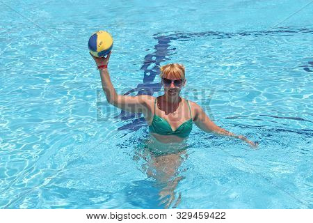 Hurghada / Egypt. 02 August 2018:
Cheerful Woman In Sun Glasses With Ball For Rugby Swimming In Pool