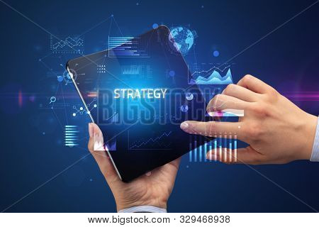 Businessman holding a foldable smartphone with STRATEGY inscription, successful business concept