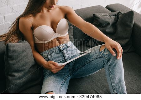 Cropped View Of Woman In White Bra And Jeans Using Digital Tablet On Sofa