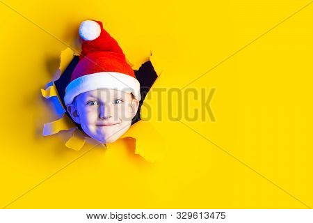 Little Cheerful Santa In A Hat Smiles, Getting Out Of The Ragged Yellow Background Lit By Neon Light