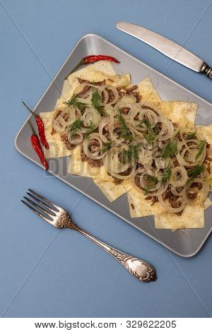 Beshbarmak Is A National Kazakh Dish - Square Pasta With Boiled Meat And Onions. On A Blue Backgroun