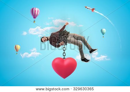 Man In Blue Sky Bound With Chains To Huge Red Heart Which Is Pulling Him Down.