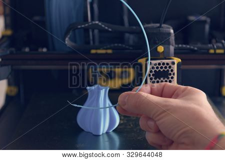 Modern 3d printer with printed three dimentional model of vase. Hand holding filament in the foreground