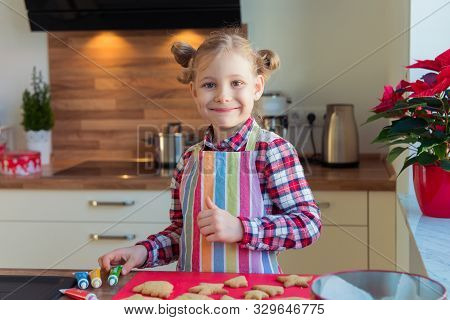 Portrait Of Pretty Little Girl With  Funny Pigtails Decoraiting Christmas Cookies