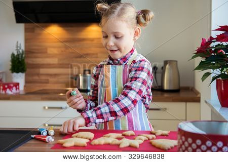 Pretty Little Girl With Funny Pigtails Decoraiting Christmas Cookies Of Different Forms In Kitchen