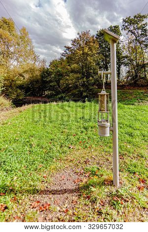 Old Lantern Of An Old Coal Mine, Placed Next To A River In The Forest, Reference Point In The Histor