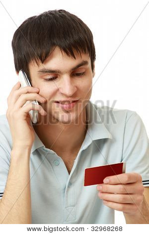 A young man with a credit card in front of a laptop, talking on the phone, isolated on white
