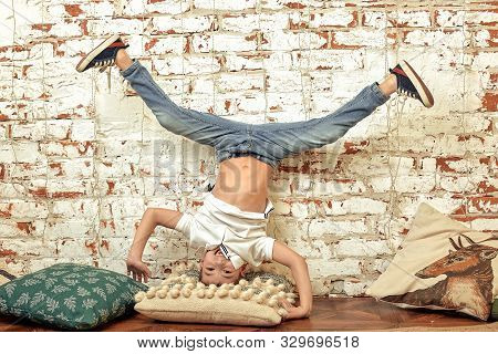 A Boy Stands Upside Down Against A Brick Wall. A Bored Boy Stands On His Head. Brick Background, Ent