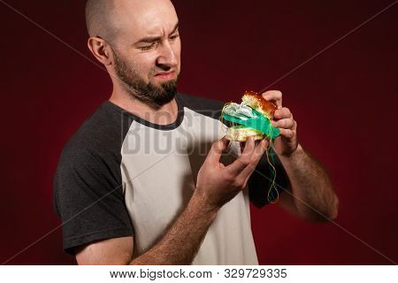 The Concept Of Fast Food And Ecology. A Bald Man With A Beard Looks Disgustedly Into The Plastic Fil