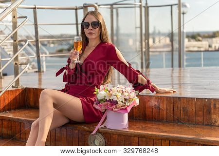 Woman Is Sitting On Cruise Liner Deck With A Bouquet Of Flowers And Drinking Wine. The Concept Of Va