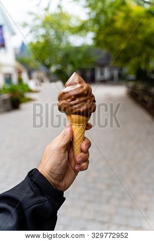 Man Holding Dipped Chocolate Ice Cream Cone In Hand, Very Blurred Background, Small Depth Of Field. 