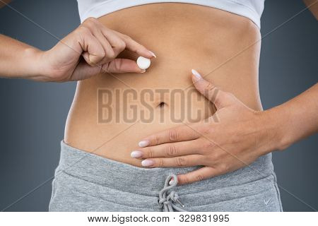 Woman Holding Pill In Front Of Her Stomach