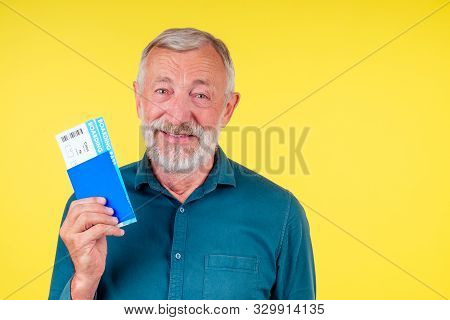 Smiling Senior Man Holding Passport In Blue Cover And Tickets Studio Yellow Background
