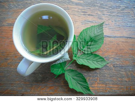 Transparent Freshly Brewed Raspberry Leaf Tea In A White Cup On A Wooden Surface And A Fresh Raspber