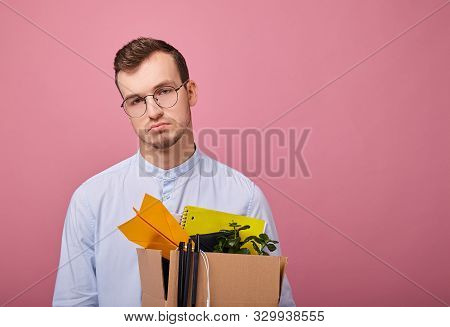 A Young Pretty Guy In A Sky Blue Shirt And Computer Glasses Stands On A Pink Background With A Cardb