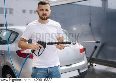 Portrait Of Handsome Man On Self Wash Station. Background Of Wet Gray Car