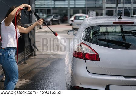 Back View Of Young Woman Cleaning Her Car On Self Service Car. Female Washing With Jet Sprayer. Whit