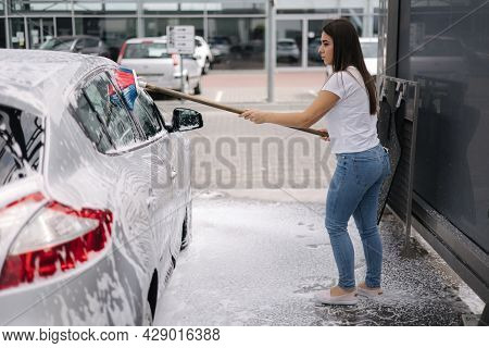 Attractive Young Woman Washing Her Car With Shampoo And Brushes. Female Washes Automobile With Foam 
