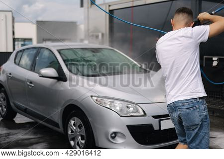 Back View Of Young Man Cleaning His Car With A Jet Sprayer. Self-service Car Washing