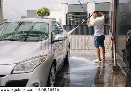 Young Man Cleaning His Car With A Jet Sprayer. Self-service Car Washing