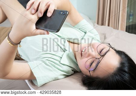 Beautiful Glasses Asian Woman Lie On Her Back, Chatting, Typing, And Texting, Mobile In Her Bedroom 