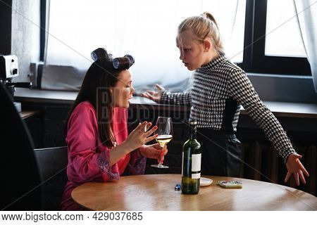 Alcoholism in family problem. Daughter aguring with her mother about drinking wine. Two people, woman and teenage girl quarrel in the kitchen. A depressed female is addicted to alcohol at home.