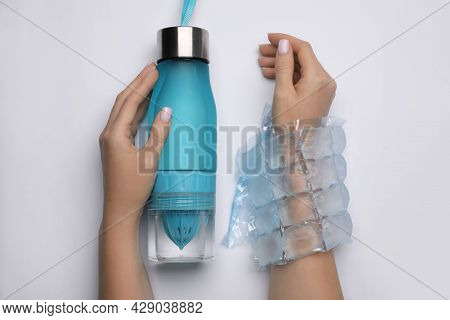 Woman With Ice Pack And Bottle Of Water On White Background, Top View. Heat Stroke Treatment
