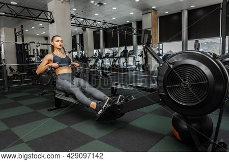 Young Cross Fit Woman Works Out In A Rowing Machine At Modern Gym. Functional Training. Healthy Life