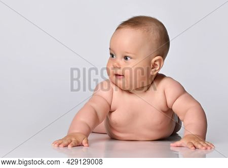 Six-month-old Baby In One Diaper Stands Up On The Arms And Looks To The Side, Against A Light Backgr