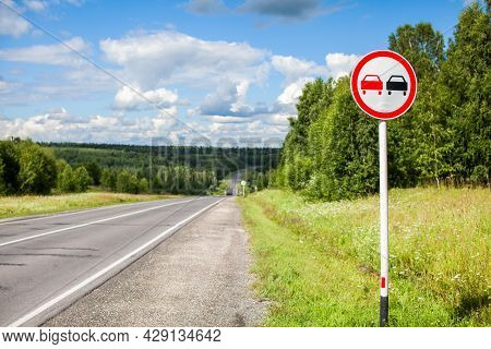 A Road Sign Overtaking Is Prohibited On A Suburban Highway Through The Forest On A Sunny Summer Day.