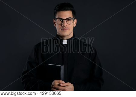 Priest In Cassock With Bible On Black Background
