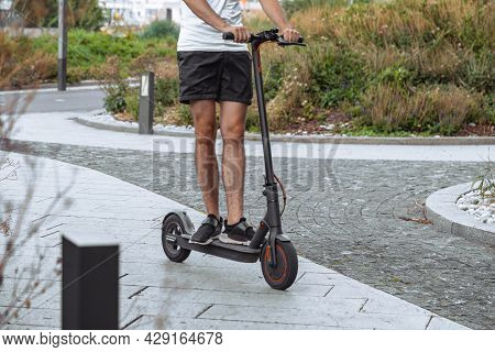 Close Up Of Young Man Riding Black Electric Kick Scooter At Cityscape