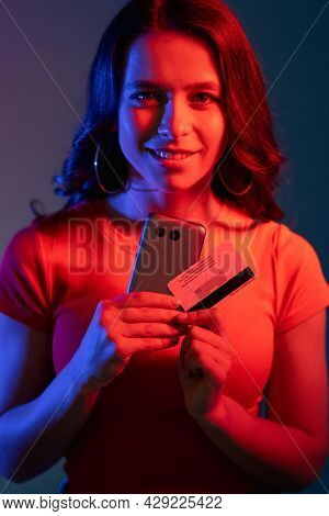 Secure Payment. Cyber Banking. Internet Shopping. Cheerful Smiling Woman In Neon Bright Red Blue Col