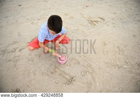 High Angleview Of A Happy, Handsome And Adorable Boy, Child, Toddler Filling Toy Bucket With Sand Fo