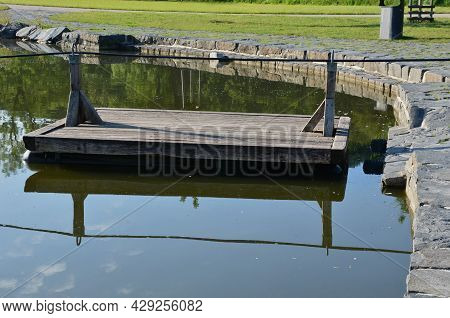 A Wooden Raft Is Tied To A Taut Rope. Self-service Ferry Across The River, Pond. People Get On And P