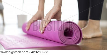 Young Woman Rolling Her Yoga Mat After Exercising And Doing Meditation At Home
