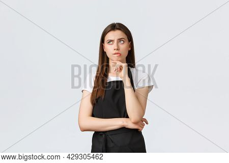 Small Business, Employees And Coffee Shop Concept. Complicated Thougtful Saleswoman In Black Apron T