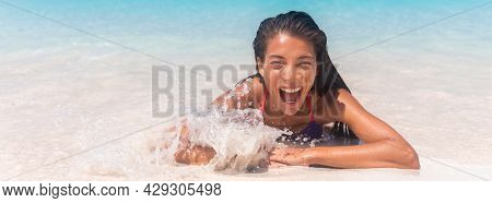 Summer fun happy woman swimming in ocean wave in beach surprised funny from wave splash sunbathing in Caribbean travel vacation. Panoramic banner of holiday.