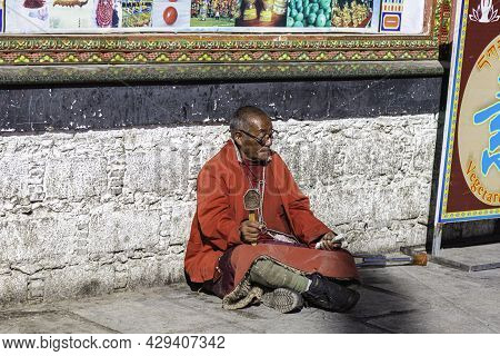 Lhasa, Tibet, China - November 15, 2019: Old Tibetan Man  With  Crutches And Tibetan Prayer Wheel Si