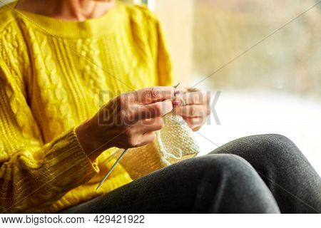 Mature Female Sitting On The Windowsill And Knitting