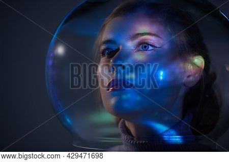 Beautiful tender girl with blue eyes in a glass spacesuit looks into the distance against the background of outer space. Space concept. Copy space. 