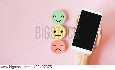 Hand Holding White Mobile Phone With Clipping Path On Touch Screen, Above Emotion Face On Sweet Pink