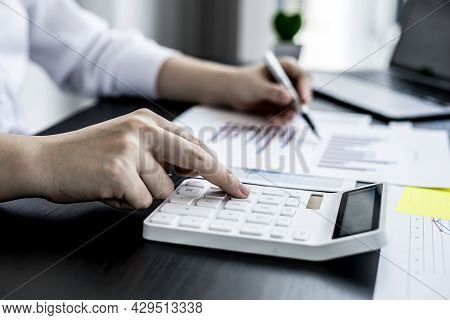Close-up Of Woman Holding A Pen And Pressing A White Calculator, A Corporate Finance Auditor Examini