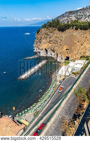 Sorrento, Italy - August 26 2020: Small Beach Full Of Colorful Sunbeds And Umbrellas Next To High Cl