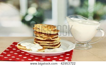 หวาน pancakes บนแผ่น ด้วยครีมเปรี้ยวบนโต๊ะในห้องครัว