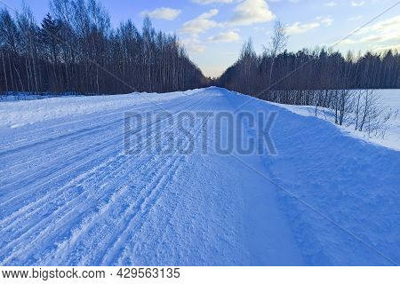 Snow-covered Country Road Through The Fields After A Blizzard At Sunset. Winter Rural Scene. Dramati