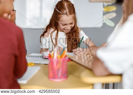Happy Girl Sitting At The Table And Writing In A Notebook