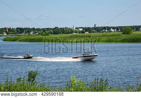 Latvia, Jurmala, August, 2021 - Motor Boat Rides Of People On Inflatable Sofa Down The Lielupe River