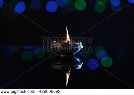 Lit Diya On Dark Background With Blurred Lights. Diwali Lamp