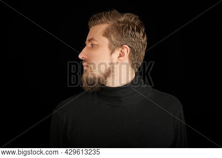 Cute Bearded Man, Half-face Portrait, Black Background. Young Guy In Black Polo Neck Sweater. Confid